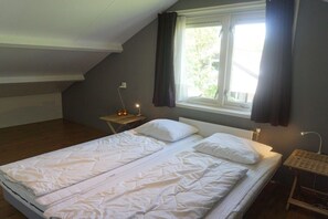 A single-bed room with a sloped ceiling, a window with curtains, a bedside table with a lamp, and a radiator. - Merel, De Keizerskroon 93 (Julianadorp aan Zee)