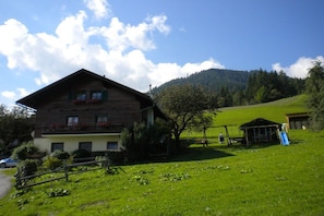 Un chalet en bois doté d’un balcon, entouré d’un champ verdoyant et luxuriant, avec une montagne en toile de fond.