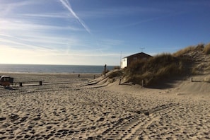 Een zandstrand met voetafdrukken, een houten constructie en een heldere lucht.