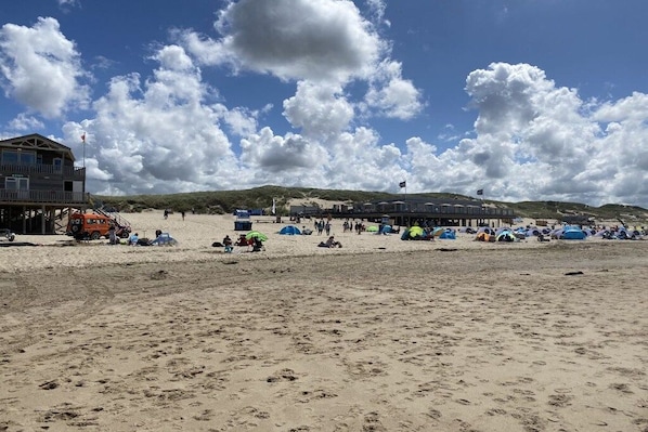 Een strand met een uitkijktoren voor strandwachten, strandparasols en tenten.