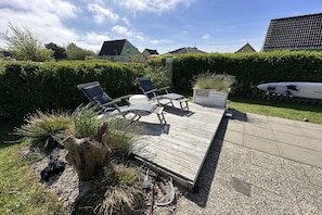 Een houten terras met twee ligstoelen en een plant in pot.