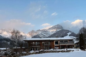Un bâtiment de style chalet doté d’un balcon, entouré de montagnes et d’arbres couverts de neige.
