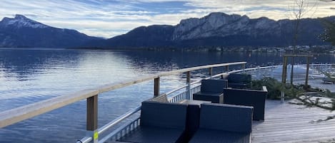 A deck with outdoor seating overlooking a calm lake and mountains.