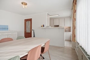 Une pièce comprenant une table à manger, des chaises, un coin cuisine et une porte.