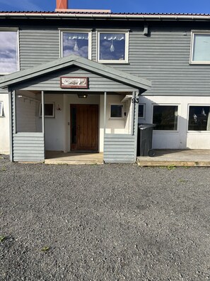 A two-story building with a porch, a wooden door, and a sign indicating it's an apartment. - Solhaug apartment, Fredvang (Flakstad)