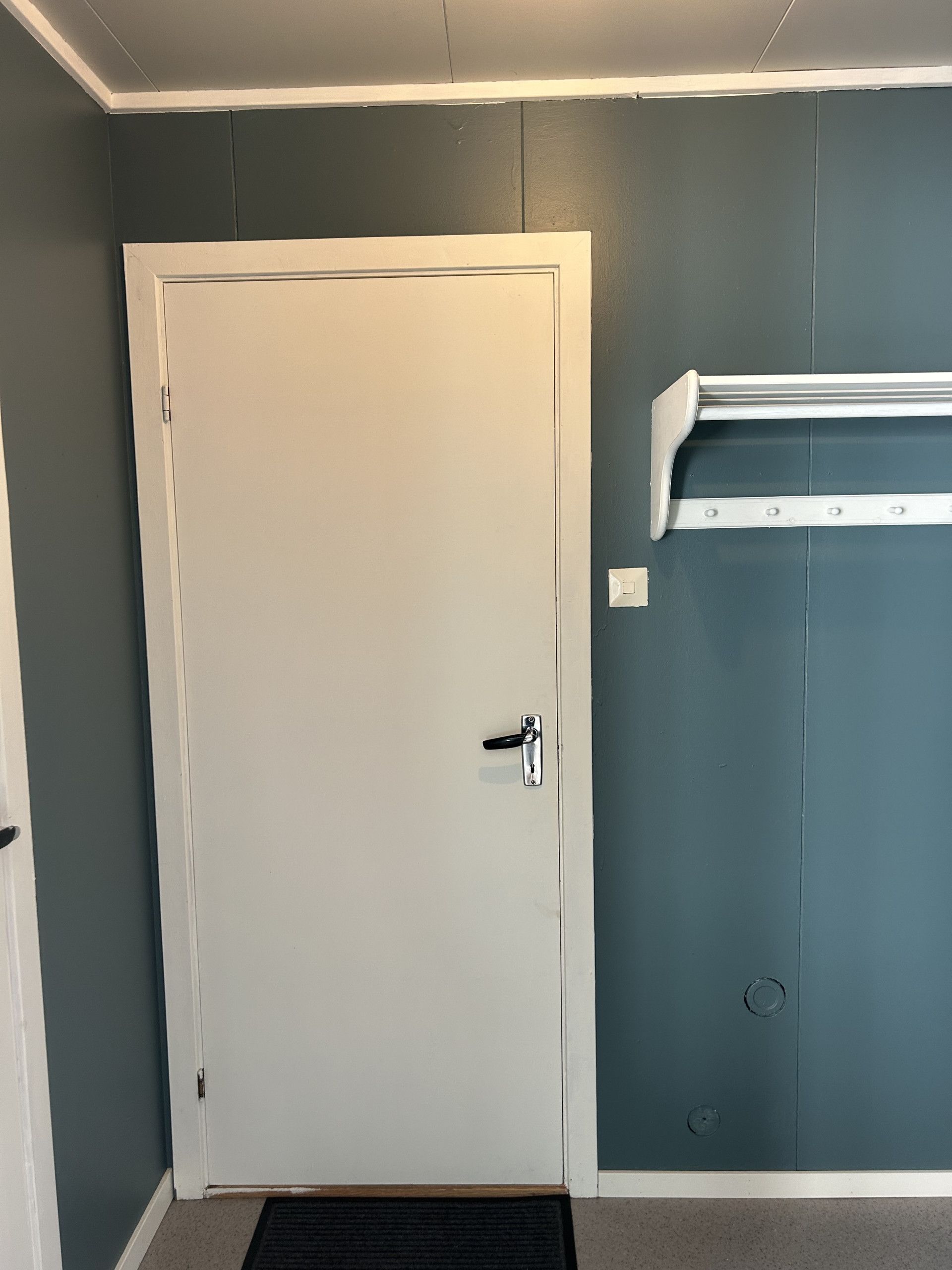 A closed door with a handle, a white baseboard, and a wall-mounted shelf.