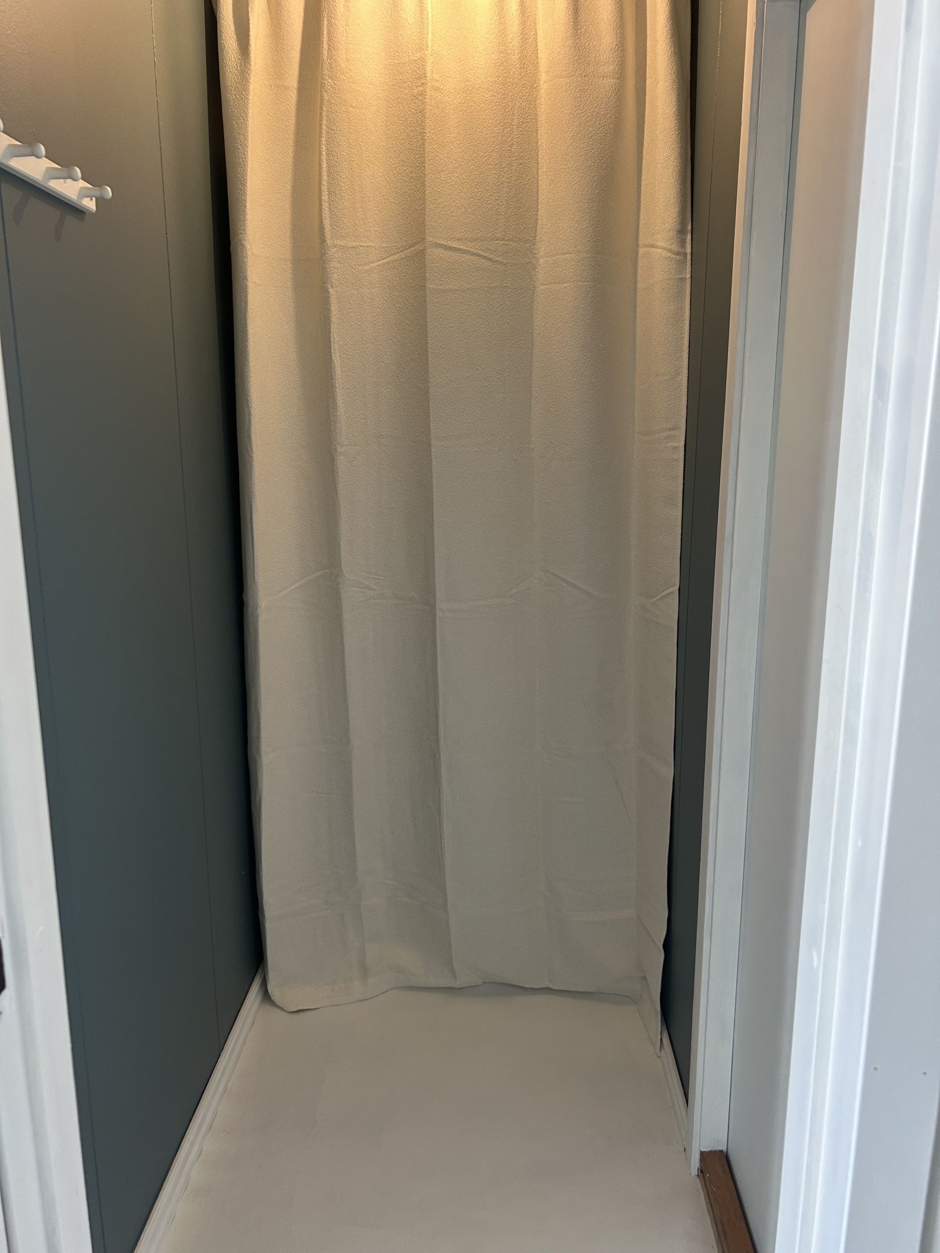 Een smalle gang met een beige gordijn, een witte deuropening en een witte muur.