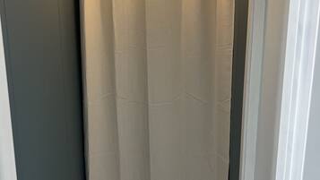 Een smalle gang met een beige gordijn, een witte deuropening en een witte muur.