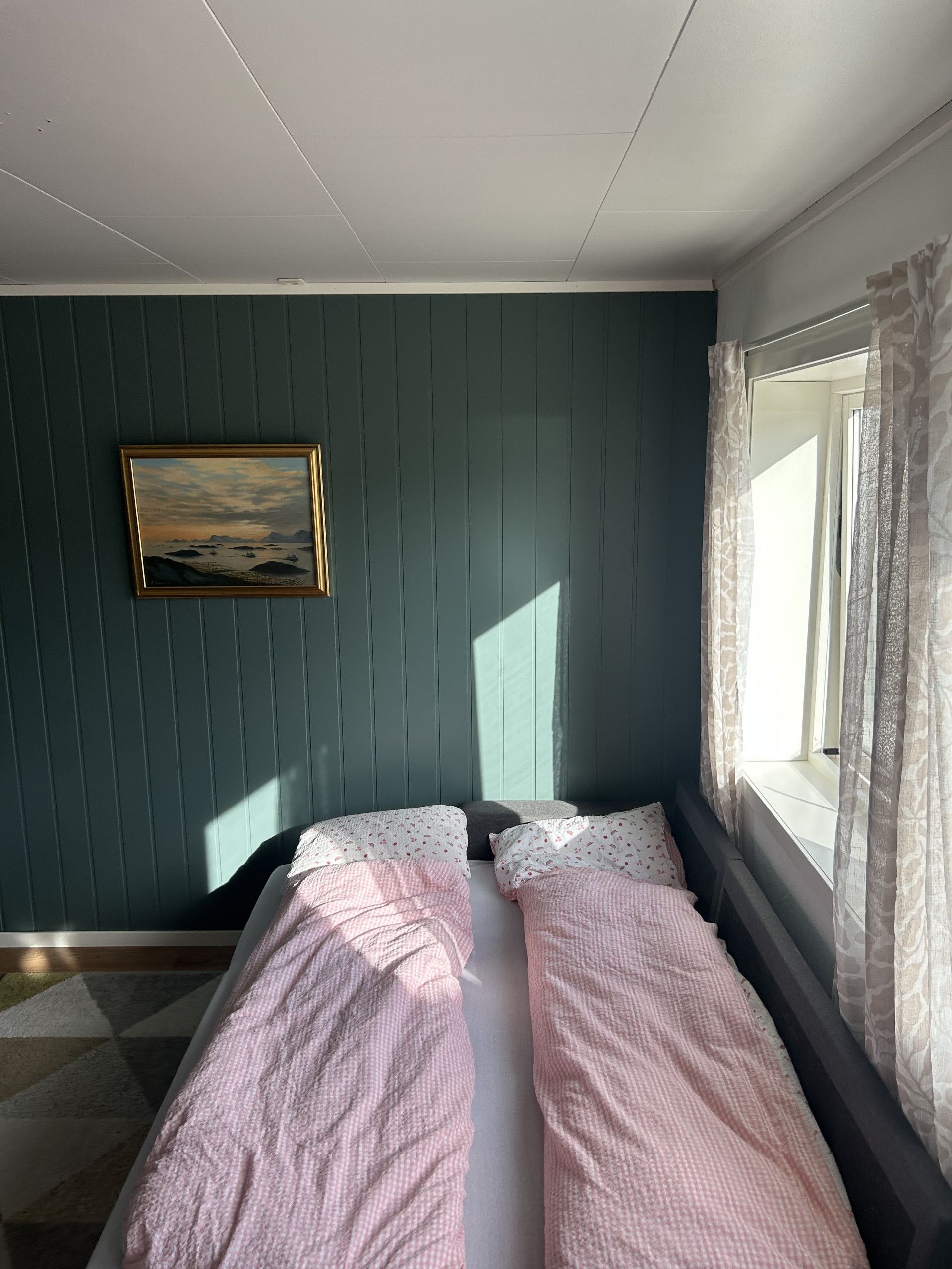 A room with a bed, a painting on the wall, and a window with curtains.
