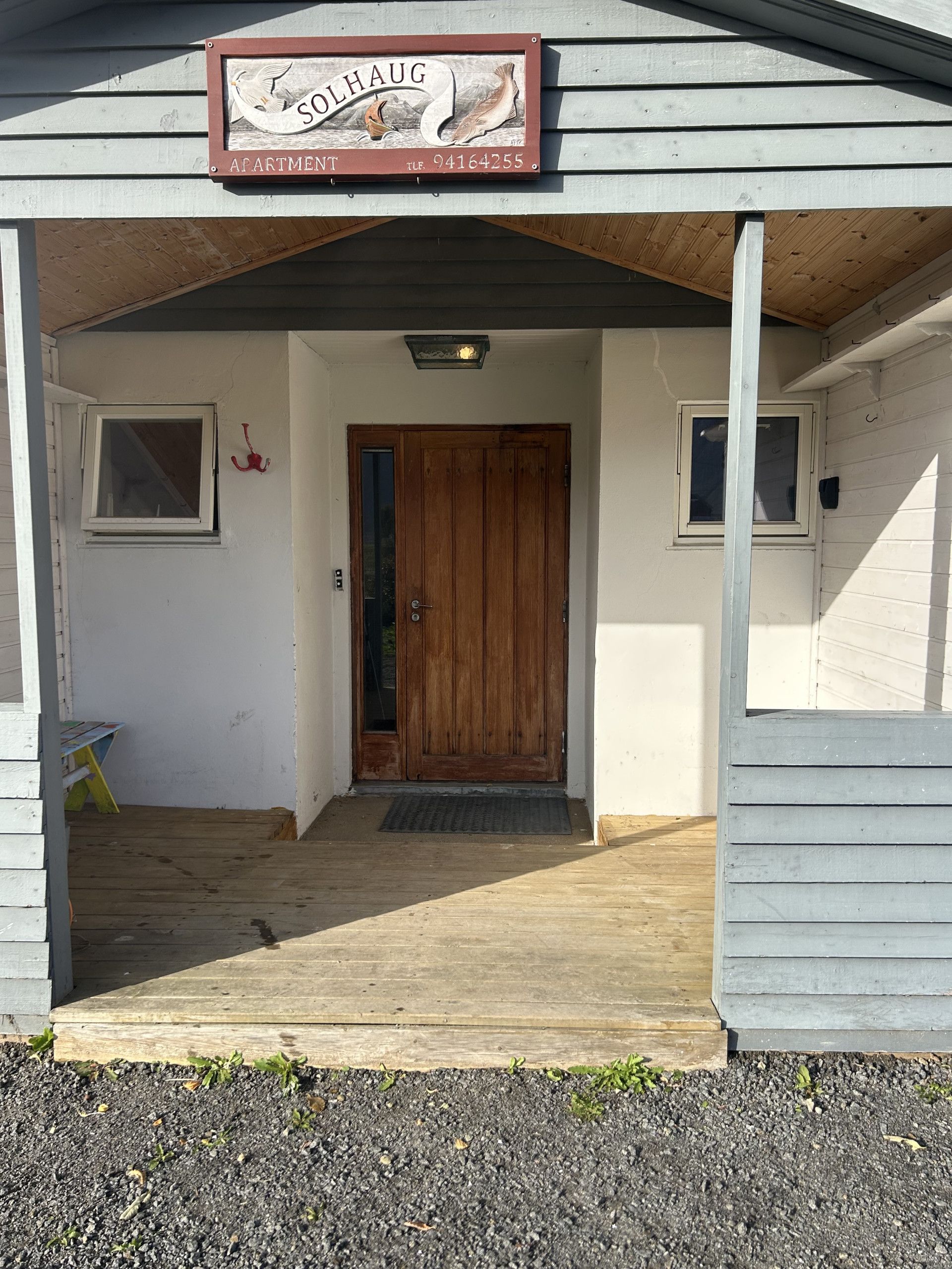 A wooden building with a sign reading 'SOLAUG APARTMENT' and a contact number.