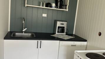 Een kleine keuken met witte kastjes, een zwart aanrecht, een koffiezetapparaat, een waterkoker en een fornuis.