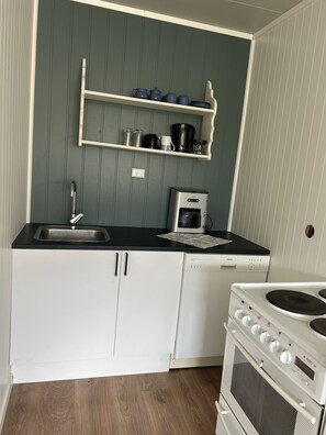 A compact kitchen with white cabinets, a black countertop, a coffee maker, a kettle, and a stove. - Solhaug apartment, Fredvang (Flakstad)