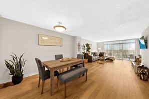 A spacious living area with a wooden dining table, grey upholstered chairs, a sofa, and a large window with blinds. - Fantastic 2-bedroom apartment with AC in Marina del Rey (Marina del Rey)