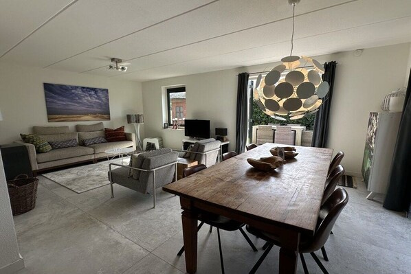 Een moderne woonkamer met een eethoek, een zithoek, een flatscreen televisie en een opvallende hanglamp.