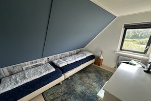 Een kamer met een schuine kap, een bed met hoofdeinde, een raam en een radiator.