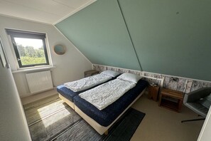 Een slaapkamer met een schuine kap, een raam, een bed met twee kussens, een nachtkastje en een stoel.