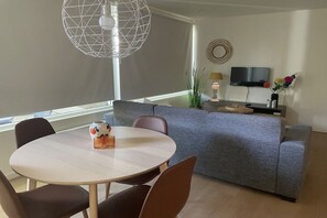 A modern living room with a round dining table, grey sofa, and a TV mounted on the wall. - Holiday apartment with 3 bedrooms (Callantsoog)