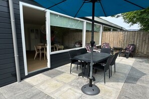 An outdoor patio with a table and chairs, a blue umbrella, and a wooden fence. - Holiday apartment with 3 bedrooms (Callantsoog)