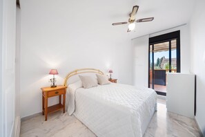 Ein Schlafzimmer mit einem Bett, Nachttischen, einem Deckenventilator und Blick durch eine Glastür.