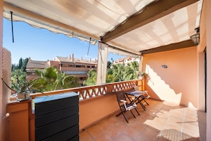 Ein Balkon mit Tisch und Stühlen, einem Blumentopf und Blick auf Gebäude im Hintergrund.