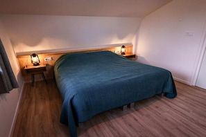 Ein Schlafzimmer mit einem Einzelbett, einem Holz-Kopfteil, zwei Nachttischen mit Lampen und einem Holzboden.