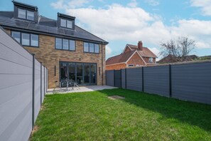 A residential property with a brick house, a fenced backyard, and a patio area with outdoor furniture. - Luxaura Homes 6 Bed Detached House (Maidenhead)
