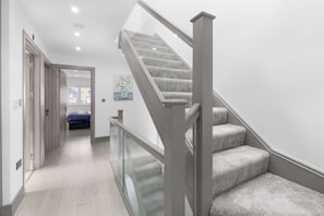 Ein modernes Interieur mit Teppichstufen, einem Gang zu einem Schlafzimmer und einem Glasgeländer.