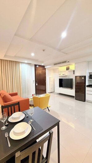 A modern living room with a sofa, dining table set for two, and a kitchen area with appliances. - TC Contel at Charan Phrom Phong - Ginger (Bangkok)