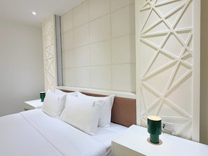 A hotel room with a large bed, white bedding, a headboard with geometric patterns, a bedside table with a green lamp, and a wall panel with a similar design. - TC Contel at Charan Phrom Phong - Ginger (Bangkok)