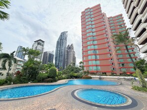 A swimming pool with a tiled edge, surrounded by greenery and palm trees, with high-rise buildings in the background. - TC Contel at Charan Phrom Phong - Ginger (Bangkok)