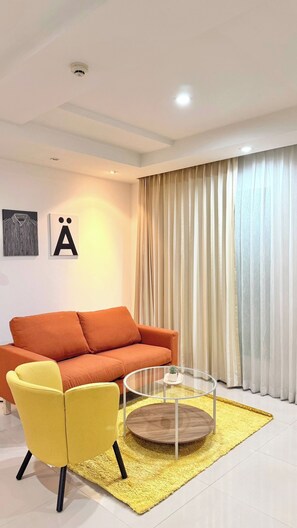 A modern living room with a sofa, a yellow chair, a glass coffee table, and a large window with curtains. - TC Contel at Charan Phrom Phong - Ginger (Bangkok)