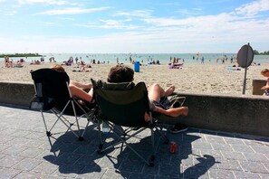 Eine Strandansicht mit Menschen, die am Sand entspannen und Stühlen entlang des Gehwegs.