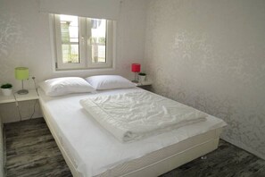 Ein Schlafzimmer mit einem Bett, einem Fenster, einem Nachttisch mit Lampe und einer Wand mit dezentem Muster.