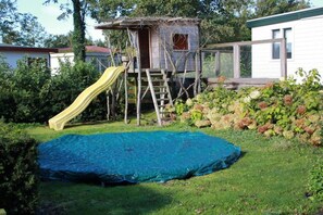 Un jardin avec une cabane en bois, un toboggan et un trampoline.
