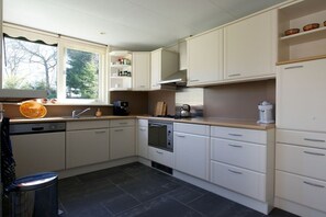 A kitchen with white cabinets, a dishwasher, a stove, and a window with a view of trees.