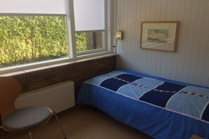 A bedroom with a single bed, a chair, a radiator, a window with a view of trees, and a painting on the wall. - "Holland House" at De Zandloper (Julianadorp)