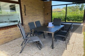 An outdoor patio with a table and chairs, a brick wall, and a view of greenery. - "Holland House" at De Zandloper (Julianadorp)