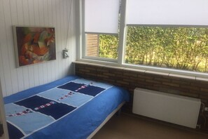 Ein Zimmer mit einem Einzelbett, einem Heizkörper, einem Fenster mit Jalousien und einem Bild an der Wand.