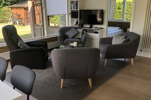 En moderne stue med sofa, lænestole, sofabord og tv.
