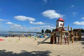 Ein Strand mit einer Holzspielanlage, einer Rutsche und Zelten im Hintergrund.