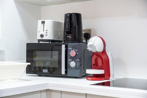 Et køkken med mikrobølgeovn, brødrister og kaffemaskine på en bordplade.
