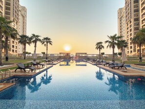 A swimming pool with lounge chairs and palm trees, surrounded by high-rise buildings. - StayShort - Superb 3BR in Palm Jumeirah With Unmatched Views for 5! (Palm Jumeirah)