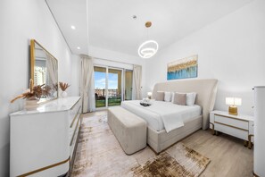 A modern hotel room with a large bed, a bedside table with a lamp, a mirror, and a view of the city through the window. - StayShort - Superb 3BR in Palm Jumeirah With Unmatched Views for 5! (Palm Jumeirah)