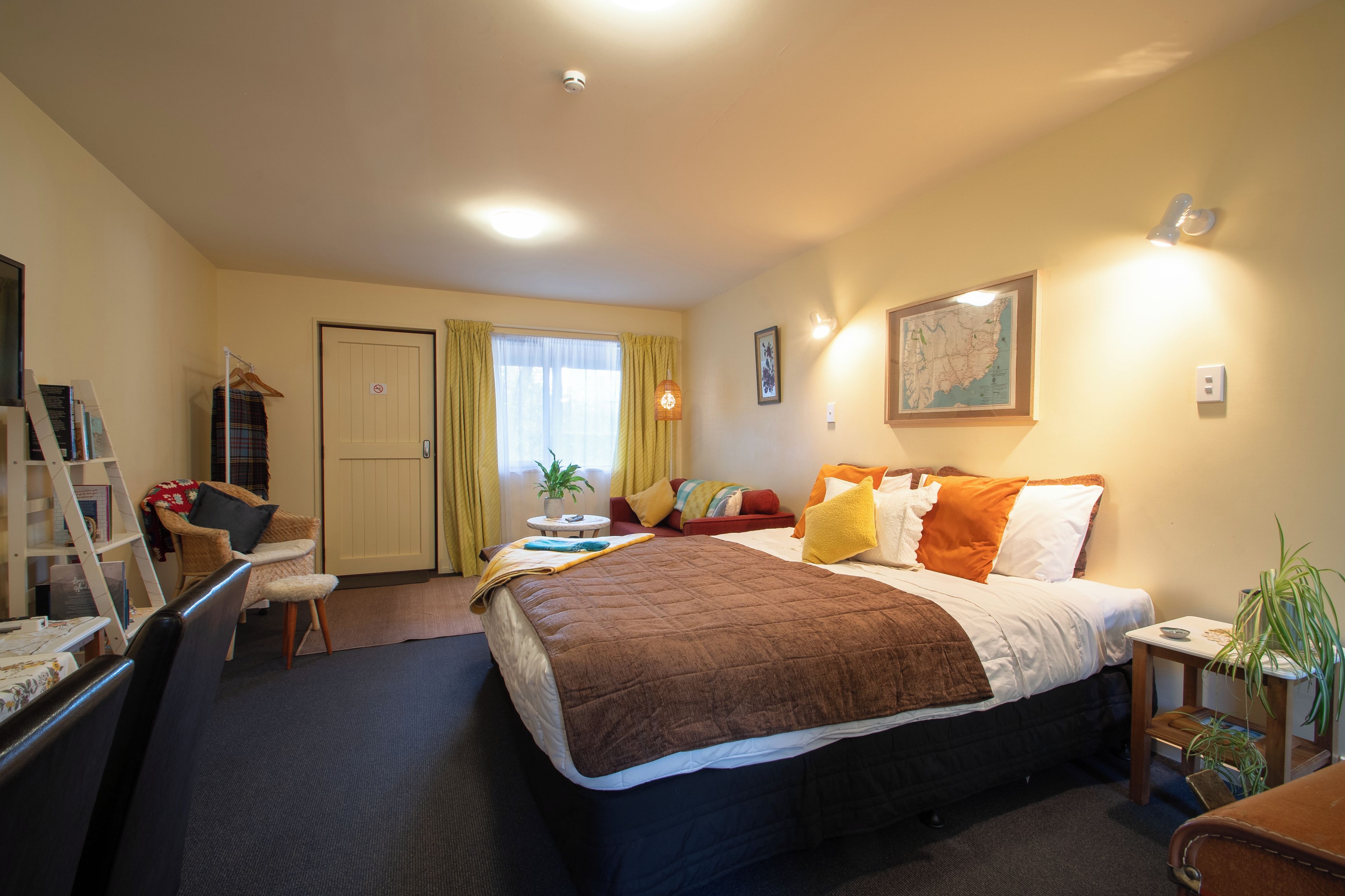 A hotel room with a bed, a desk, a chair, a wardrobe, and a map on the wall.