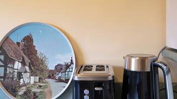 A kitchen counter with a vintage toaster, a kettle, a colander, and a framed picture of New Zealand pears.