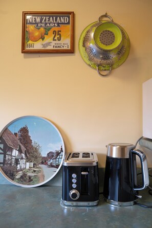 Een aanrecht met een vintage toaster, een waterkoker, een vergiet en een lijst met een afbeelding van Nieuw-Zeelandse peren.