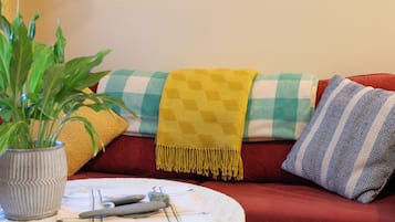 A cozy living room with a red sofa, a yellow throw blanket, a checkered pillow, a potted plant, and a hanging light fixture.