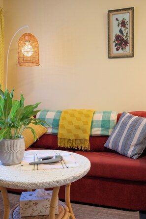 Een gezellige woonkamer met een rode bank, een gele plaid, een geruit kussen, een potplant en een hanglamp.