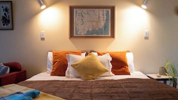 A neatly made bed with a brown quilt, multiple pillows in white and orange, and a framed map on the wall.