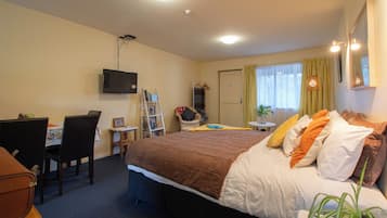 A hotel room with a bed, a desk with a chair, a television mounted on the wall, and a window with curtains.